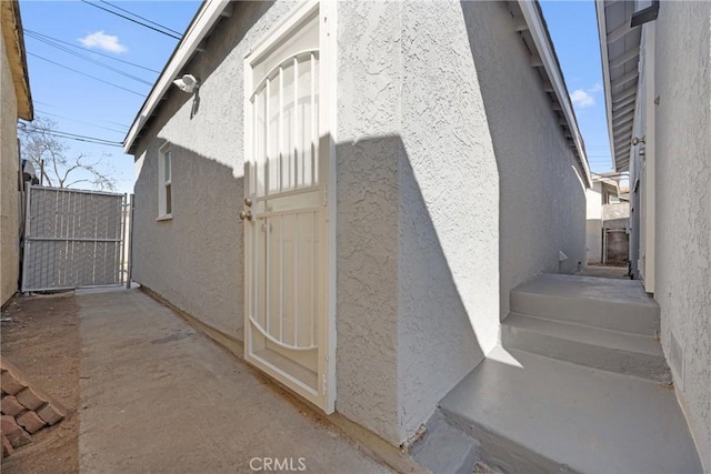 view of side of home with stucco siding and a gate