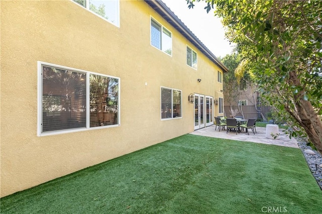 back of property featuring stucco siding, a lawn, a patio, fence, and french doors