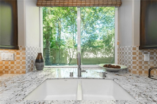 kitchen with a sink, decorative backsplash, and light stone countertops