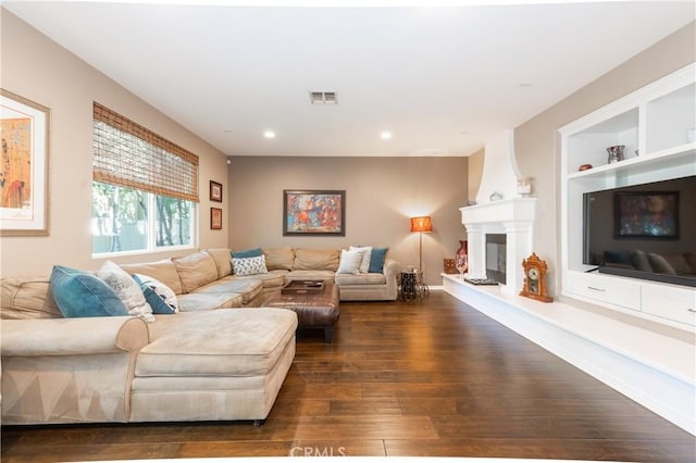 living area featuring visible vents, a large fireplace, dark wood-type flooring, built in features, and recessed lighting