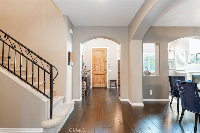 foyer entrance with baseboards, a fireplace, dark wood-style floors, and stairs