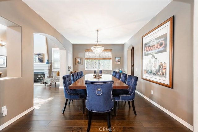 dining area with arched walkways, a fireplace, baseboards, and dark wood-style flooring