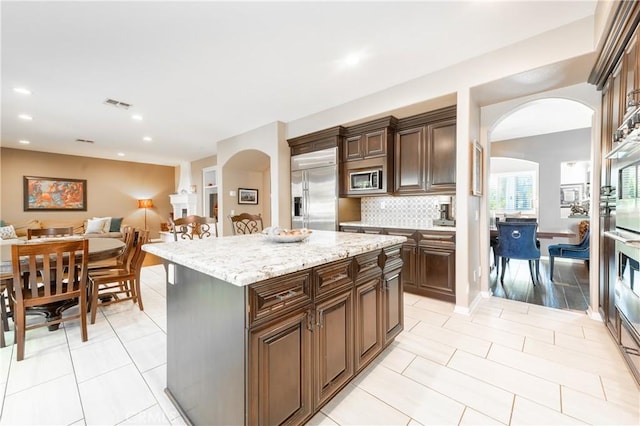 kitchen featuring tasteful backsplash, open floor plan, a center island, light tile patterned floors, and built in appliances