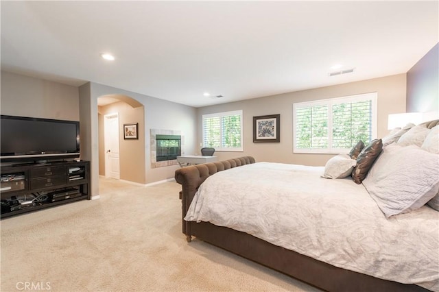 carpeted bedroom featuring visible vents, recessed lighting, arched walkways, baseboards, and a tile fireplace