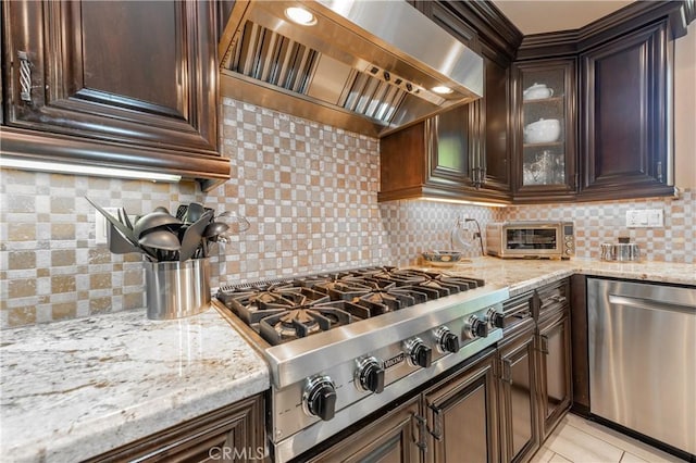 kitchen with custom exhaust hood, light stone counters, dark brown cabinets, and stainless steel appliances