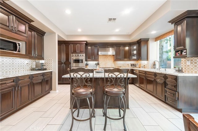 kitchen with visible vents, under cabinet range hood, appliances with stainless steel finishes, a breakfast bar area, and light stone countertops