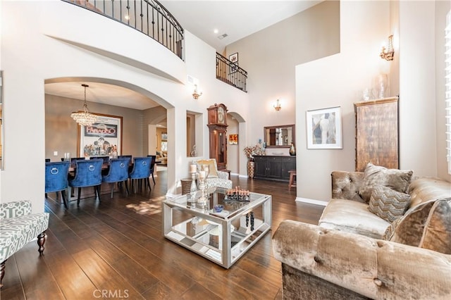 living room featuring dark wood-style floors, visible vents, baseboards, a high ceiling, and arched walkways