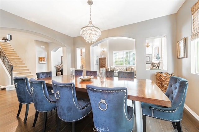 dining space with arched walkways, a notable chandelier, stairs, and wood finished floors