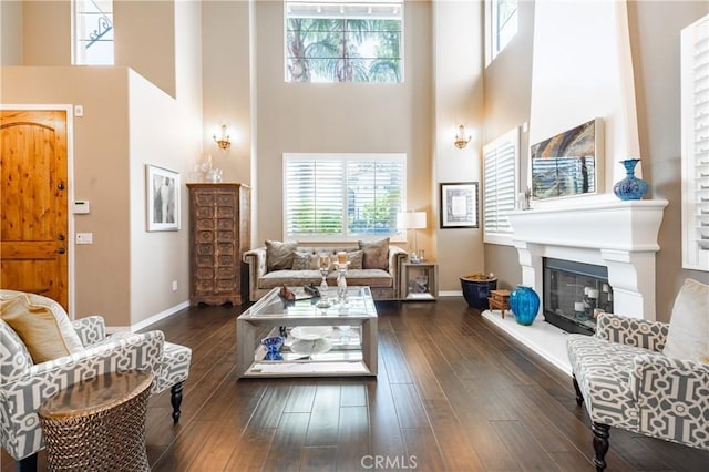 living area featuring a glass covered fireplace, a high ceiling, dark wood-style floors, and baseboards