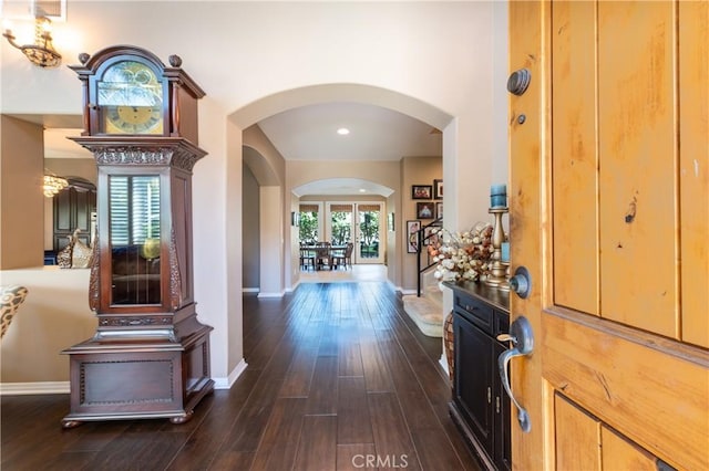 foyer entrance featuring baseboards, arched walkways, and dark wood-style flooring