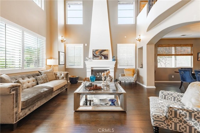 living room featuring arched walkways, a healthy amount of sunlight, wood finished floors, and a fireplace