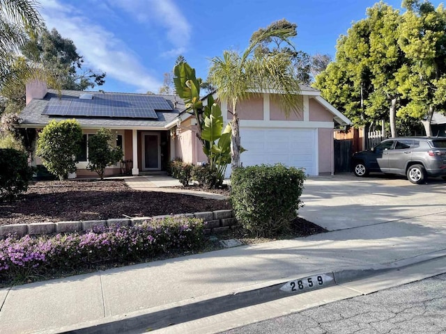 view of front facade with fence, solar panels, stucco siding, concrete driveway, and a garage