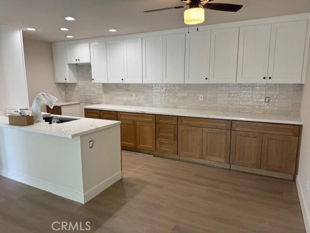 kitchen with decorative backsplash, white cabinetry, light wood-style floors, and a sink