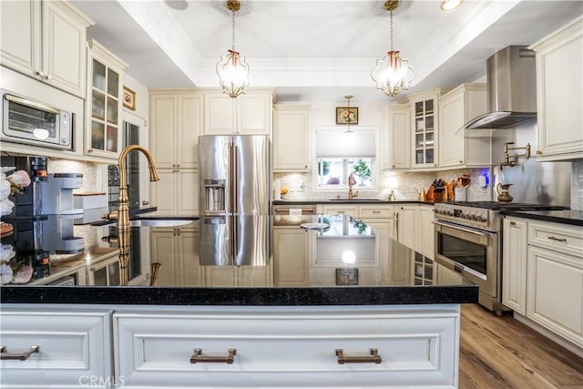 kitchen with high end appliances, a sink, decorative backsplash, a raised ceiling, and wall chimney exhaust hood