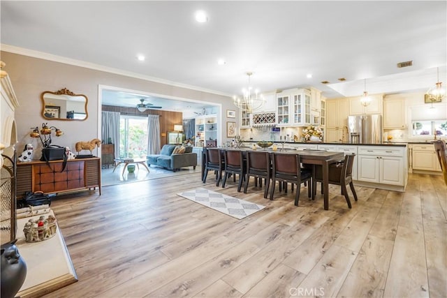 dining space with light wood finished floors, visible vents, a chandelier, and ornamental molding