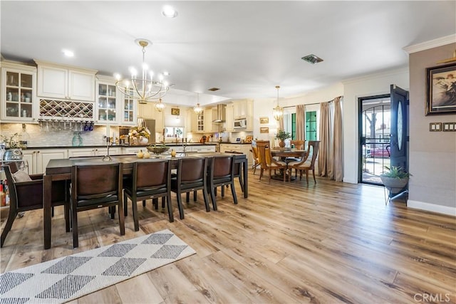 dining area featuring visible vents, baseboards, light wood finished floors, crown molding, and a chandelier