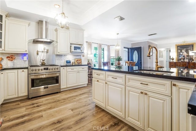 kitchen with a sink, stainless steel range with gas cooktop, dark countertops, and wall chimney range hood