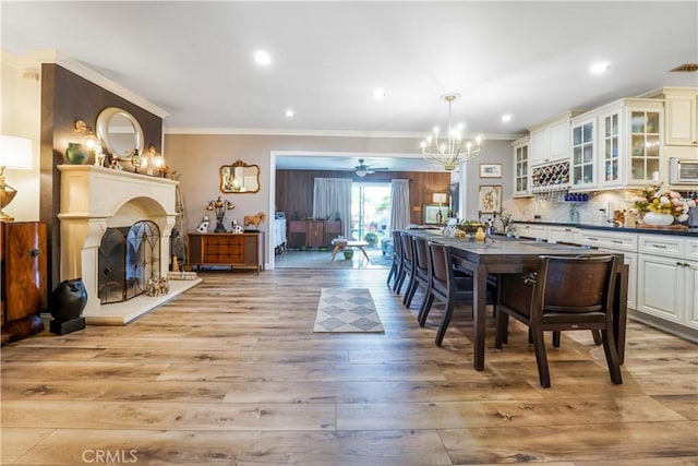 interior space featuring a fireplace with raised hearth, ornamental molding, recessed lighting, light wood-style flooring, and an inviting chandelier
