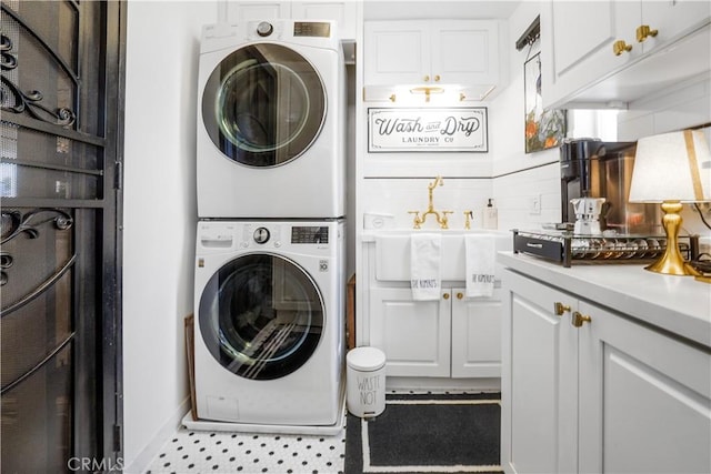 clothes washing area with laundry area, stacked washing maching and dryer, and a sink