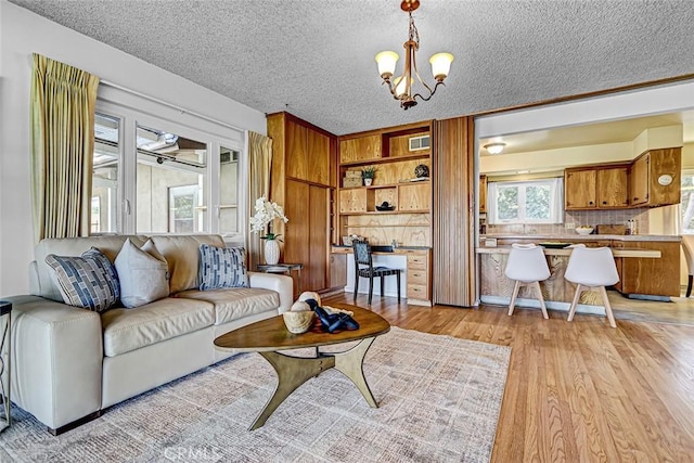 living area with a notable chandelier, a textured ceiling, built in study area, and light wood finished floors