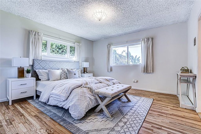 bedroom with baseboards, multiple windows, and wood finished floors