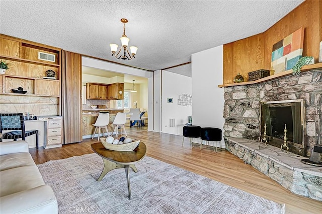 living room with visible vents, a textured ceiling, wood finished floors, a fireplace, and a chandelier