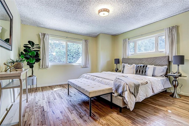 bedroom featuring baseboards, multiple windows, a textured ceiling, and wood finished floors