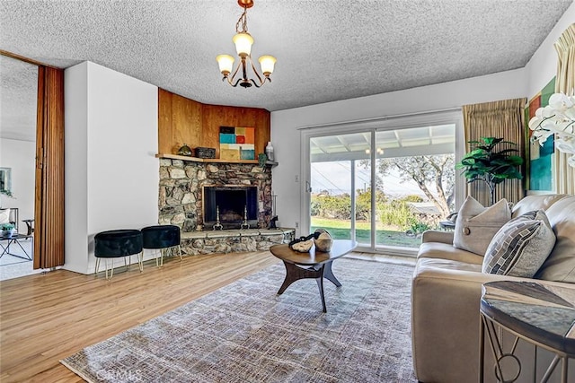 living area featuring a notable chandelier, a stone fireplace, a textured ceiling, and wood finished floors