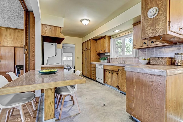 kitchen with white appliances, brown cabinets, a sink, tile counters, and tasteful backsplash