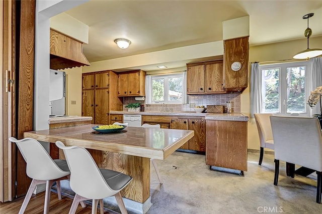 kitchen featuring decorative backsplash, brown cabinets, dishwasher, and a peninsula