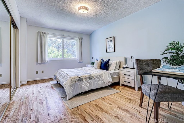 bedroom with a closet, baseboards, a textured ceiling, and light wood finished floors