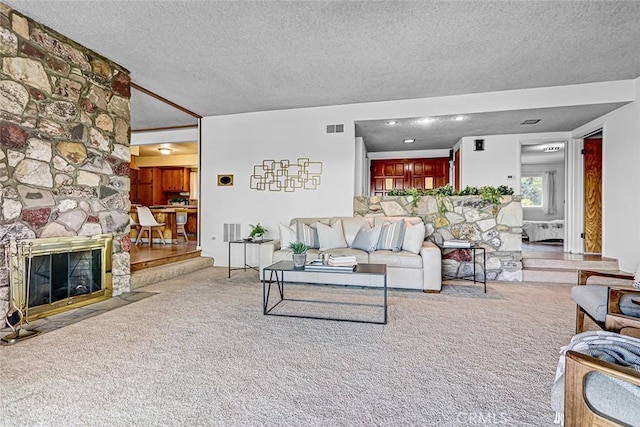 carpeted living room featuring visible vents, a textured ceiling, and a stone fireplace