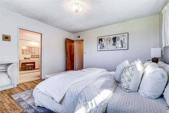 bedroom with connected bathroom, visible vents, light wood-type flooring, and a textured ceiling