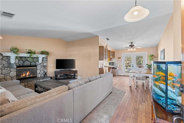 living area with visible vents, hardwood / wood-style floors, french doors, a fireplace, and vaulted ceiling