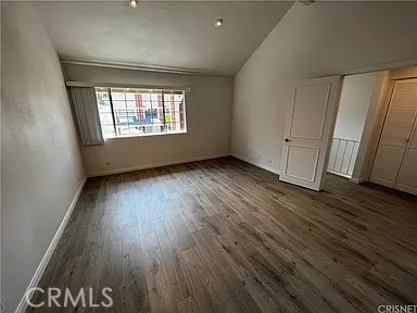 unfurnished bedroom featuring dark wood-style floors, a closet, baseboards, and lofted ceiling