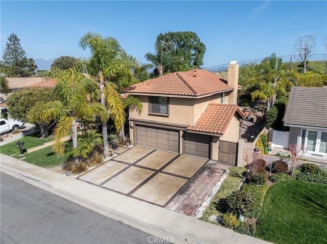 mediterranean / spanish-style home with fence, a tiled roof, stucco siding, a chimney, and an attached garage