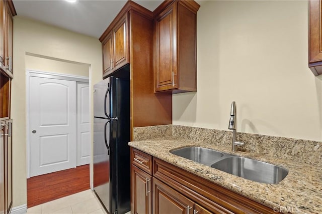 kitchen featuring light stone counters, brown cabinetry, light tile patterned flooring, freestanding refrigerator, and a sink