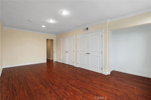 unfurnished bedroom featuring visible vents, two closets, wood finished floors, crown molding, and baseboards