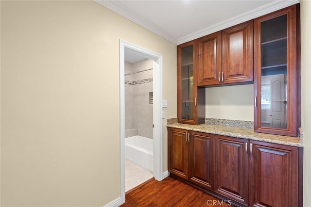 interior space featuring light stone counters, glass insert cabinets, dark wood-style floors, and crown molding