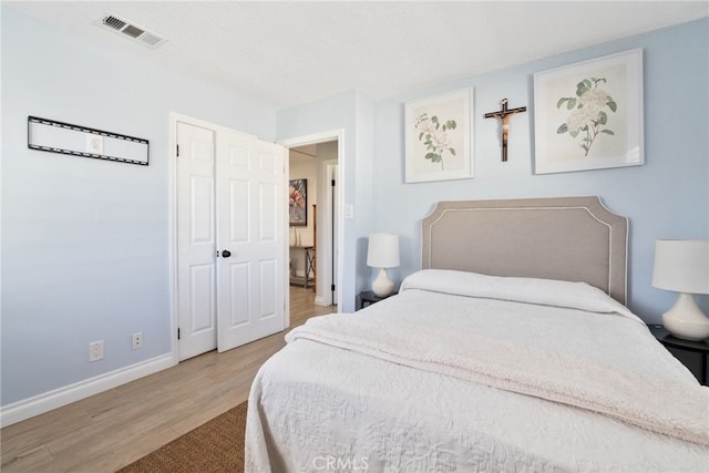 bedroom with wood finished floors, visible vents, and baseboards