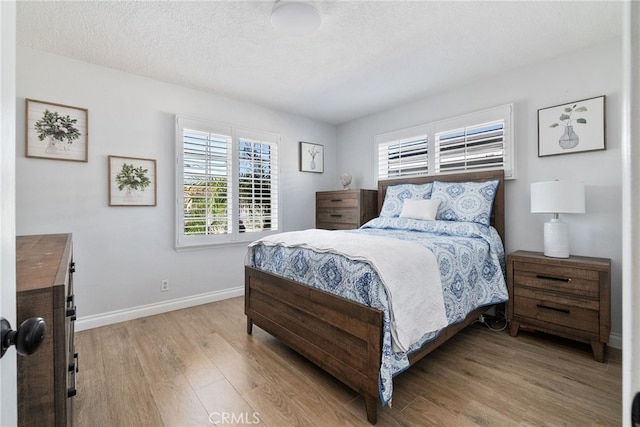 bedroom with a textured ceiling, baseboards, and light wood-style floors