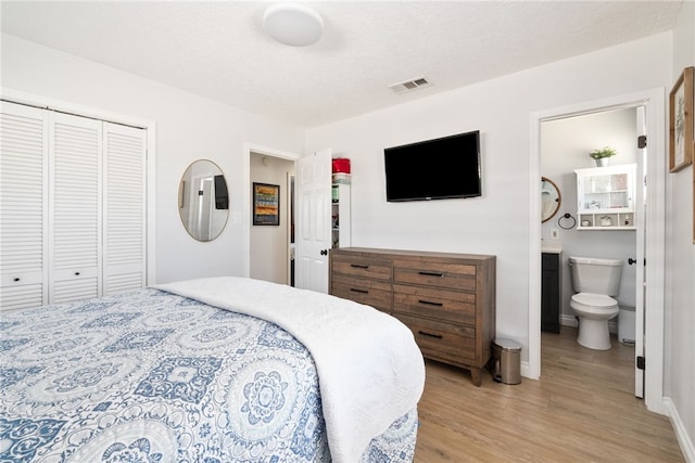 bedroom featuring visible vents, ensuite bath, light wood-style flooring, a closet, and a textured ceiling