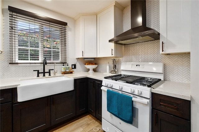 kitchen with backsplash, white range with gas stovetop, wall chimney range hood, and a sink