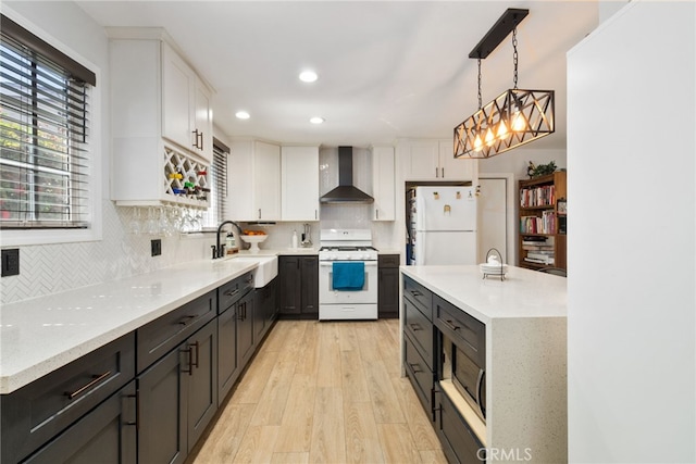 kitchen featuring white appliances, light wood finished floors, a sink, white cabinets, and wall chimney range hood