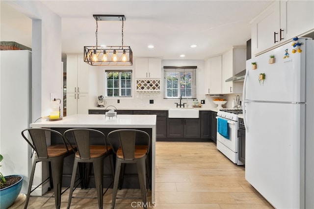 kitchen featuring white appliances, a sink, a kitchen bar, wall chimney range hood, and backsplash