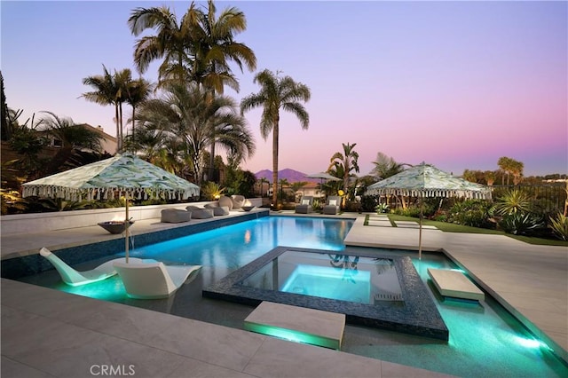 pool at dusk featuring an outdoor pool and an in ground hot tub