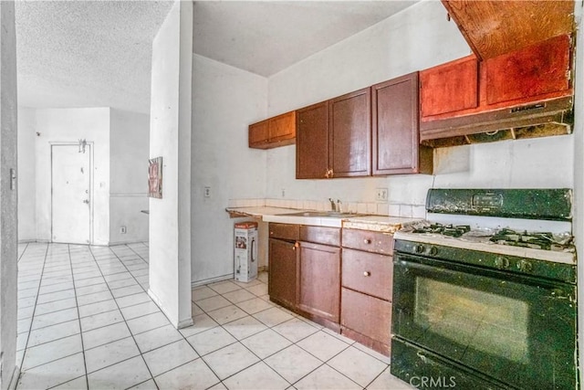 kitchen with under cabinet range hood, a sink, light tile patterned flooring, light countertops, and black range with gas stovetop