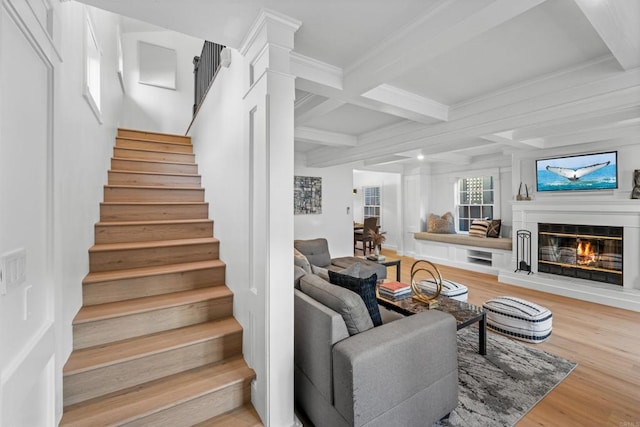 staircase featuring wood finished floors, coffered ceiling, ornamental molding, a glass covered fireplace, and beamed ceiling