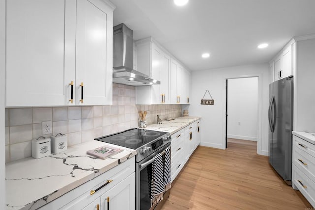 kitchen featuring tasteful backsplash, white cabinetry, stainless steel appliances, light wood-style floors, and wall chimney range hood