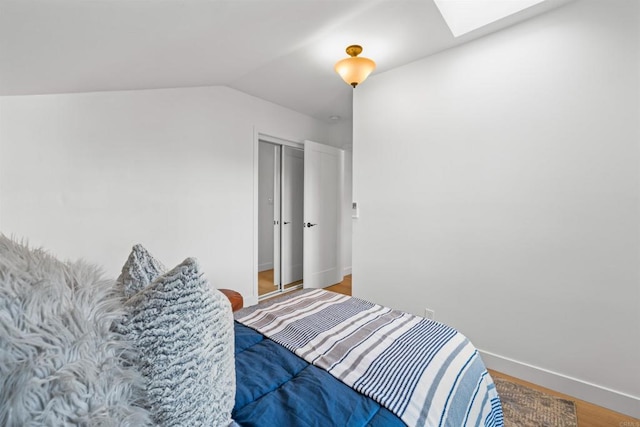 bedroom featuring lofted ceiling with skylight, wood finished floors, and baseboards